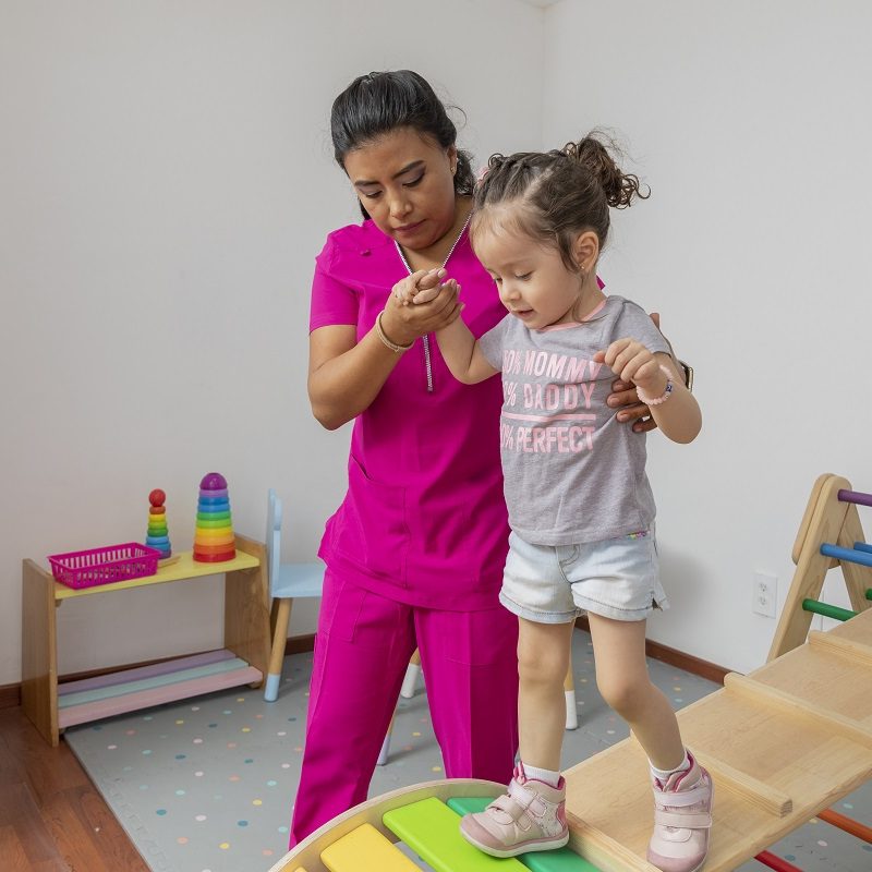 Pediatric nurse helping a girl walk through a wooden game in her medical office.